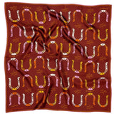 The Bandana | Big Horseshoe by Jenni Earle is a red silk scarf featuring roulottage edges and a repeating hand-illustrated pattern of yellow, pink, and white horseshoes, eyes, and lines. The scarf is slightly wrinkled.