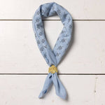 Fuck All Y'All" bandana by Jenni Earle, ethically made from hand dyed cotton, featuring a light blue pattern and displayed on a white wooden surface with a gold shell-shaped pin.