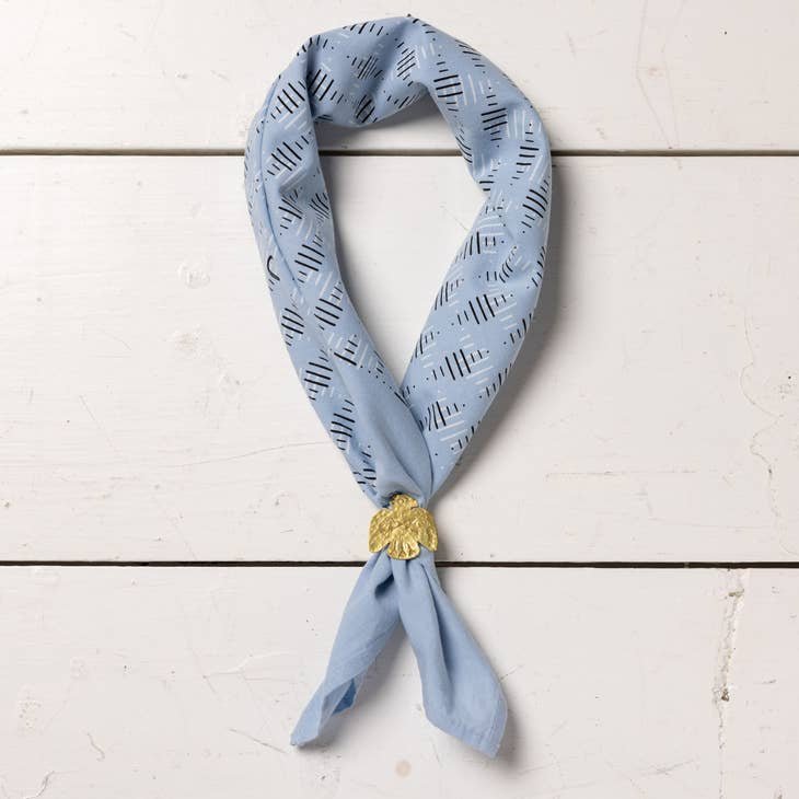 Fuck All Y'All" bandana by Jenni Earle, ethically made from hand dyed cotton, featuring a light blue pattern and displayed on a white wooden surface with a gold shell-shaped pin.