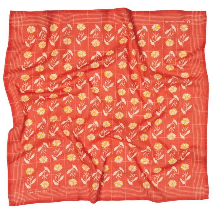 The "Hope Dies Last" square red bandana by Jenni Earle features neat rows of yellow and white flowers with green stems, creating a charming vintage western look—perfect as an inspirational gift.