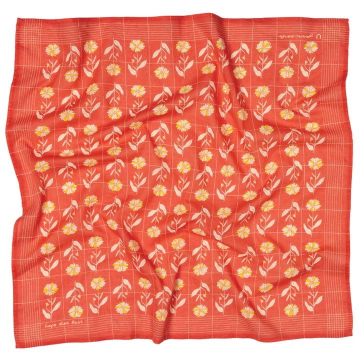 The Jenni Earle "Hope Dies Last" Bandana features a red square design with a grid pattern, yellow and white floral rows, and cursive text near two corners—ideal as a vintage western accessory or an inspirational gift.