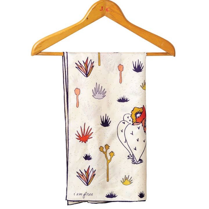 The Jenni Earle Bandana | I am Free Cactus features cream fabric hand-illustrated with orange, purple, and yellow hearts, faces, and plants. “i am free” is printed in the corner—an ideal Valentine’s Day gift.