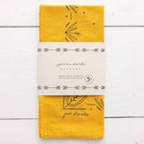 A hand-dyed yellow "Just Breathe" bandana by Jenni Earle features black line art and comes wrapped in a branded label. This western-style bandana is proudly made in the USA.