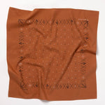 The Jenni Earle "Keep Going" bandana is a rust-colored, hand-dyed accessory with black geometric patterns and border symbols—made in the USA and perfect as a motivational gift. Shown on a white background.