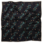 The "Lasso The Stars" bandana by Jenni Earle is a black square scarf with teal serpents, golden stars, and small dots—a magical silk accessory perfect for a distinctive holiday gift.