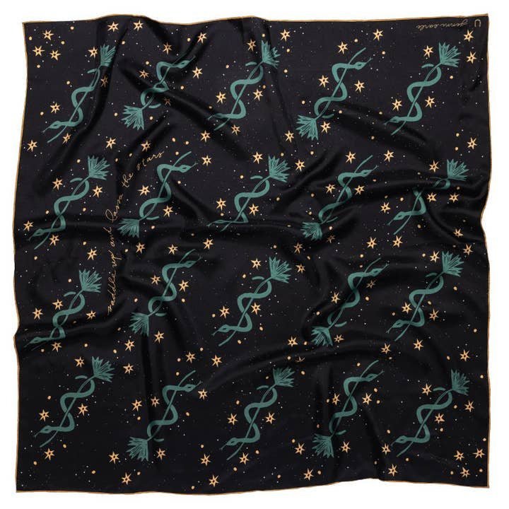The "Lasso The Stars" bandana by Jenni Earle is a black square scarf with teal serpents, golden stars, and small dots—a magical silk accessory perfect for a distinctive holiday gift.