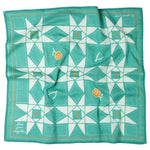 The Jenni Earle "Love Your Neighbor" bandana features a teal and white geometric star pattern with orange floral accents and the phrase "Love your neighbor" in one corner.