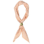 The Jenni Earle “Own Your Power” bandana is a light peach luxury cotton accessory featuring a subtle line pattern, tied in a loose knot and finished with a green decorative accent.