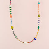 The Beaded Colorful Necklace by Jill Makes showcases an array of vibrant gemstone and Czech beads in assorted shapes and sizes, beautifully displayed on a light pink background.
