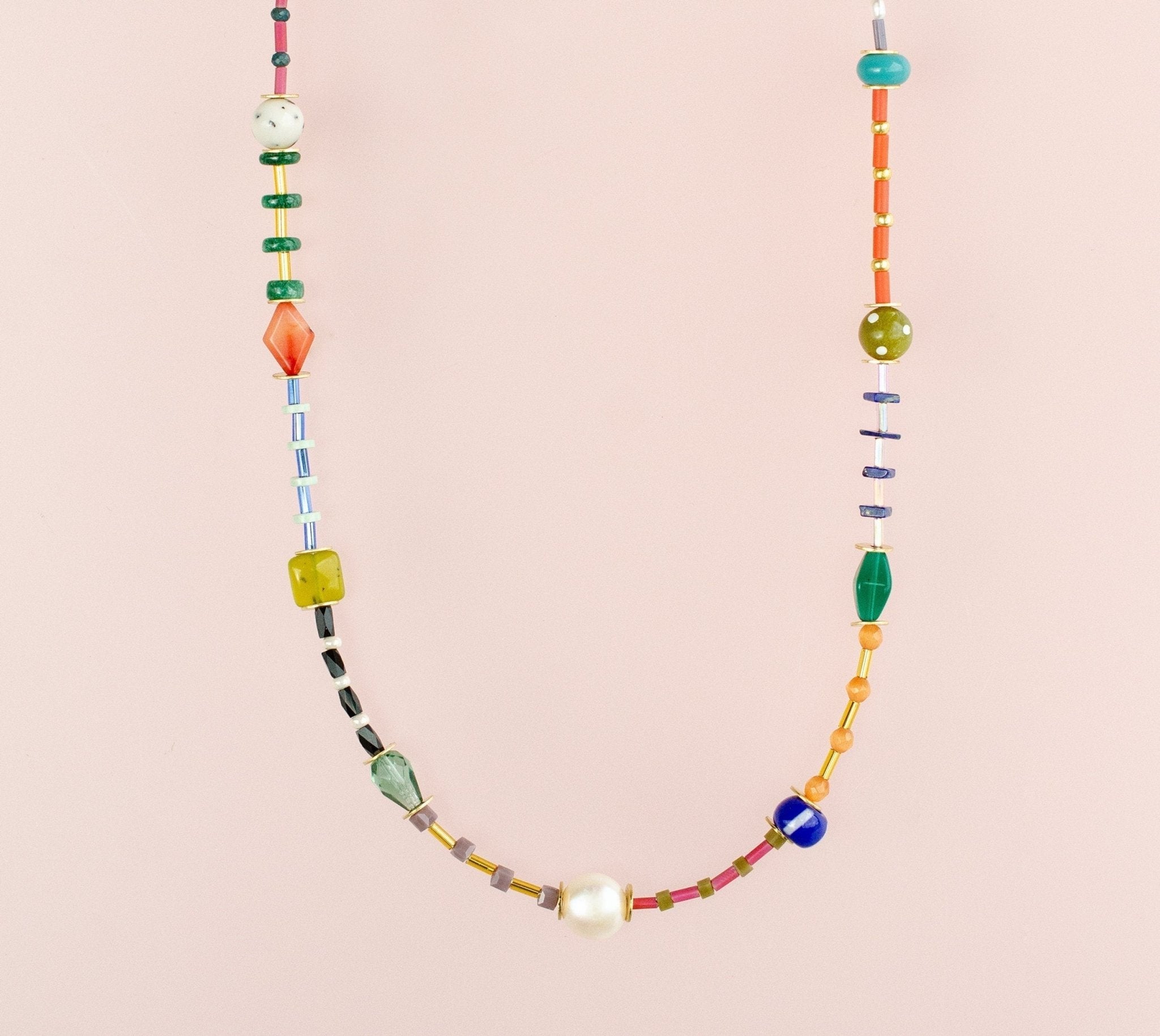The Beaded Colorful Necklace by Jill Makes showcases an array of vibrant gemstone and Czech beads in assorted shapes and sizes, beautifully displayed on a light pink background.