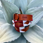 The Big Bend by Zilker Belts, crafted from hand-stitched Argentine leather and featuring a geometric "ZILKER" pattern, rests atop a pale green agave plant.