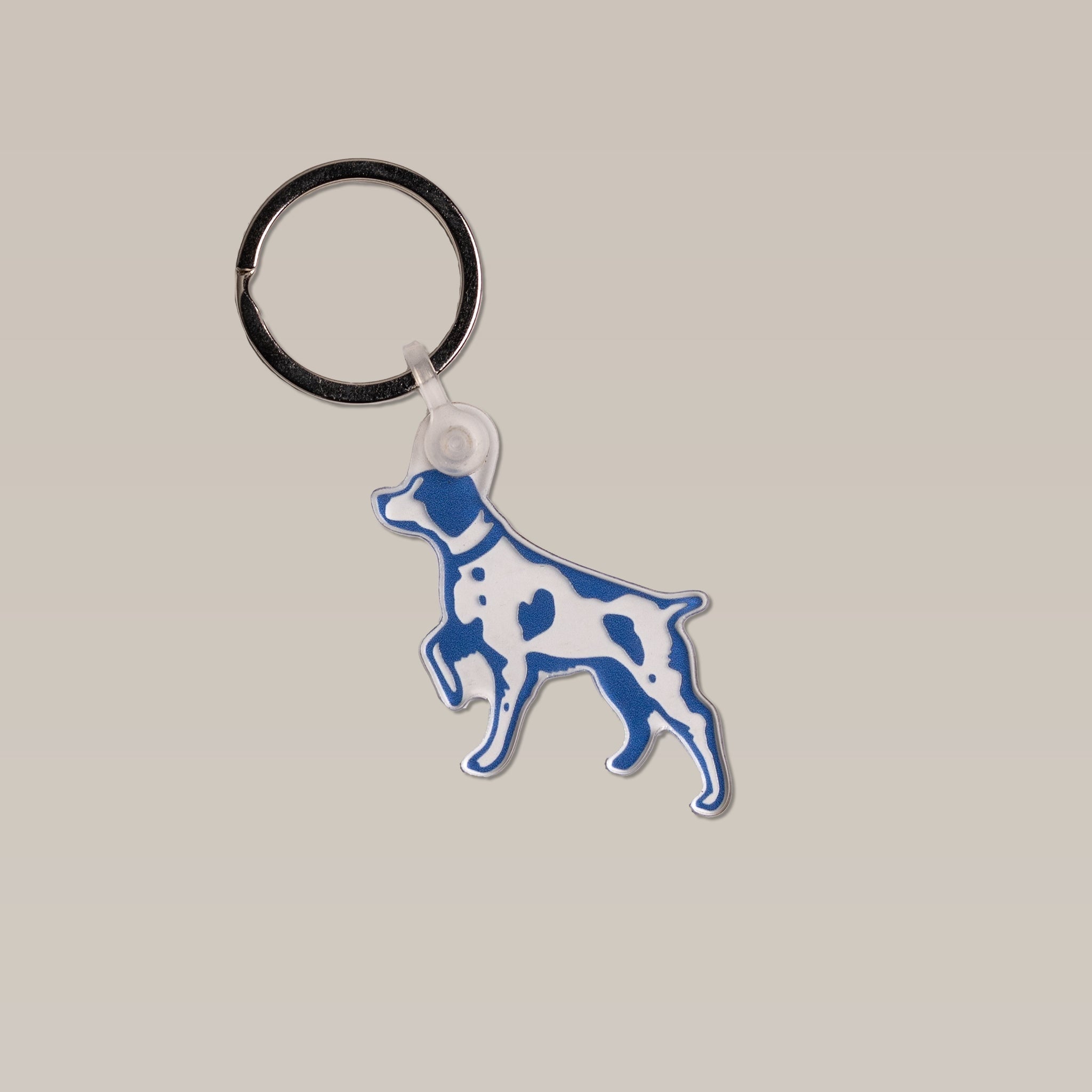 The Bird Dog Keychain by Ballad of the Bird Dog features a blue and white dog silhouette with spots, crafted from silicone with a metal key ring—perfect for outdoorsmen.