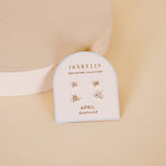 A card labeled "Birthstone Earrings | Jax Kelly" by JaxKelly displays two pairs of April birthstone earrings featuring diamond studs on sterling silver posts, set against a beige surface.