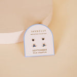 A card displaying JaxKelly Birthstone Earrings, featuring blue sapphire stones with sterling silver posts, from the brand JaxKelly, is shown on a neutral background.