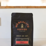 A black bag of Mescalito Coffee's Blend Whole Coffee Beans | Chilcon rests on a counter, with a blurred indoor background.