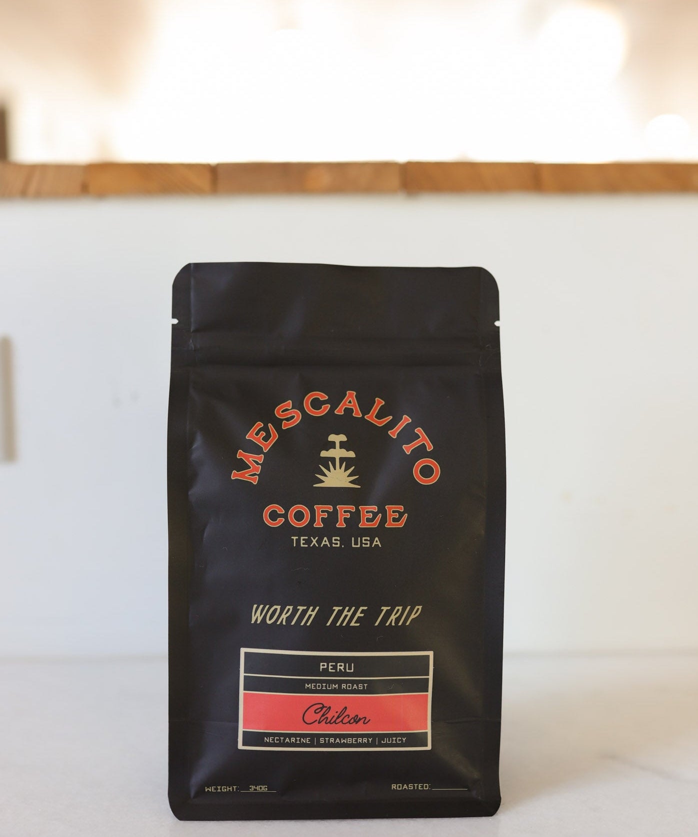 A black bag of Mescalito Coffee's Blend Whole Coffee Beans | Chilcon rests on a counter, with a blurred indoor background.