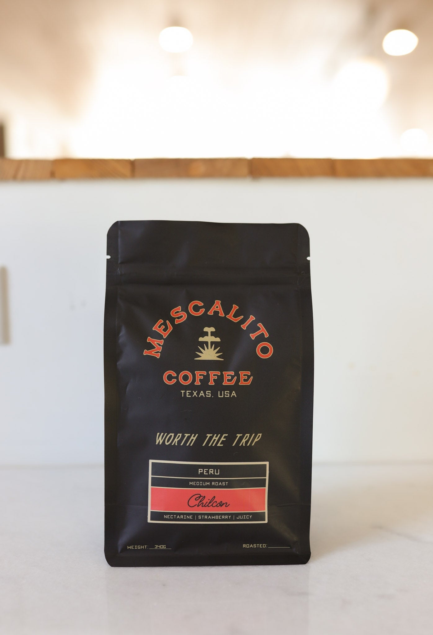 A black bag of Mescalito Coffee's Blend Whole Coffee Beans | Chilcon rests on a counter, with a blurred indoor background.