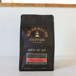 A black bag of Mescalito Coffee’s "Desert Bloom" Blend Whole Coffee Beans is a house blend roasted in Brenham, TX, featuring a medium roast with notes of desert nectarine and strawberry from Peru, El Salvador, and Ethiopia.