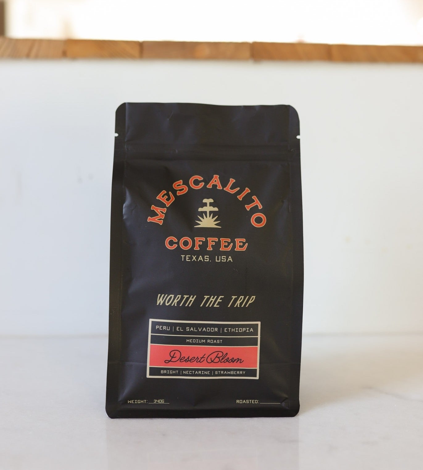 A black bag of Mescalito Coffee’s "Desert Bloom" Blend Whole Coffee Beans is a house blend roasted in Brenham, TX, featuring a medium roast with notes of desert nectarine and strawberry from Peru, El Salvador, and Ethiopia.
