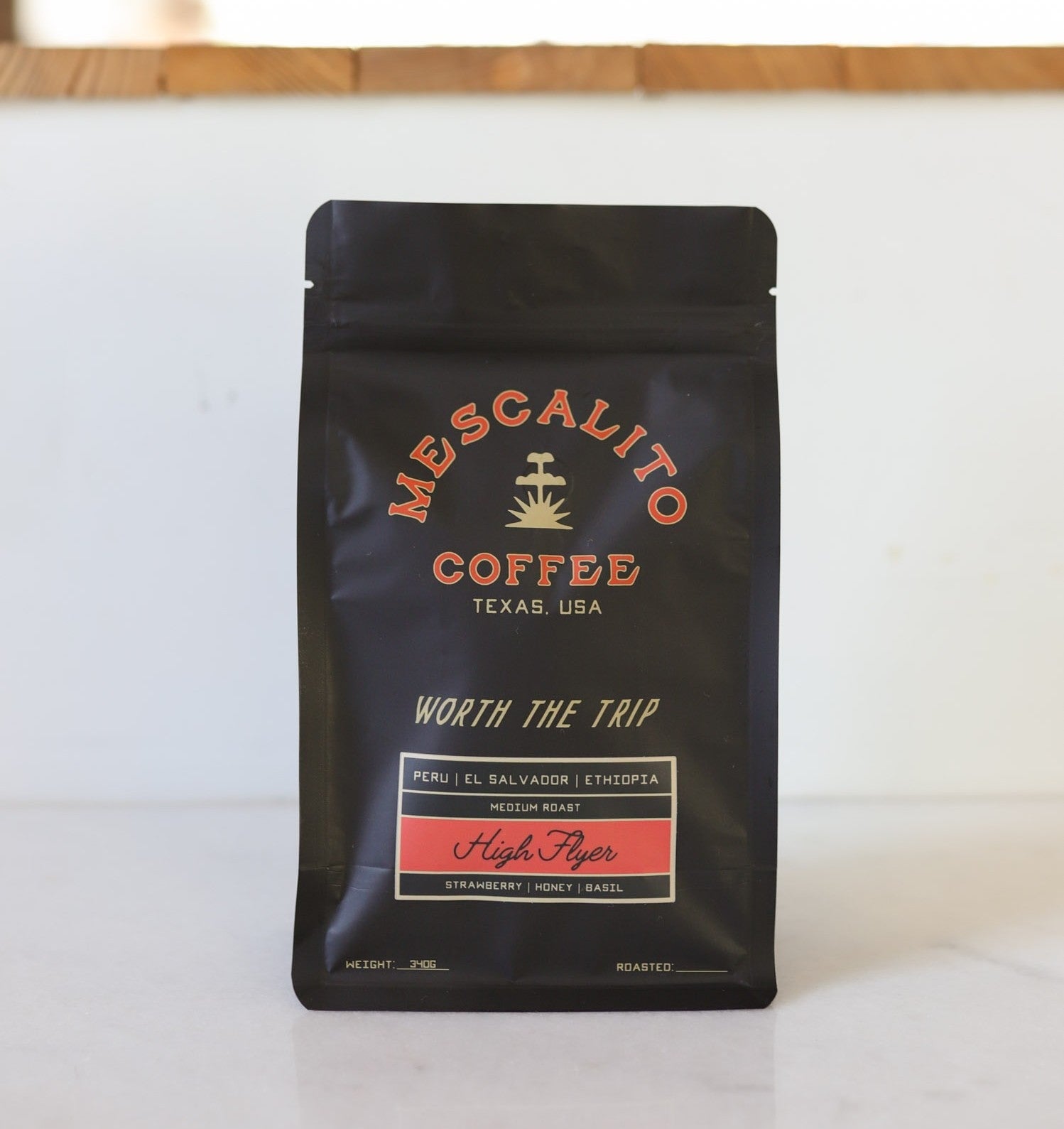 A black bag of Mescalito Coffee’s "High Flyer" blend whole coffee beans offers a medium roast crafted in Brenham, with specialty beans from Peru, El Salvador, and Ethiopia and notes of strawberry, honey, and basil.