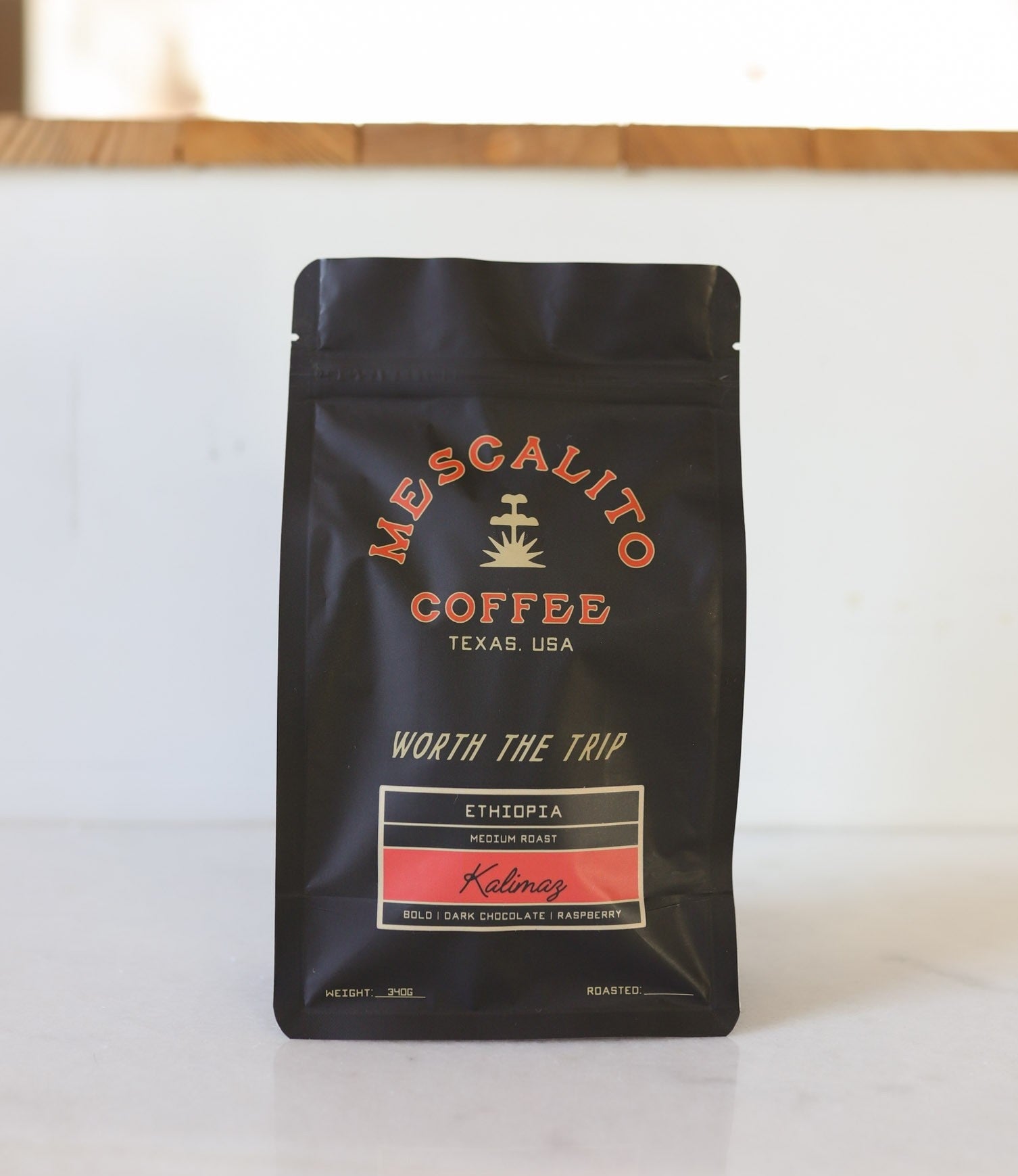 A black bag of Mescalito Coffee’s Blend Whole Coffee Beans | Kalimaz features a medium roast from Ethiopia with bold dark chocolate and raspberry notes, labeled "Worth the Trip.