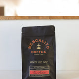 A black bag of Mescalito Coffee labeled "Blend Whole Coffee Beans | San Antonio" from Texas, USA, featuring Pacamara beans with anaerobic fermentation, sits on a white surface.