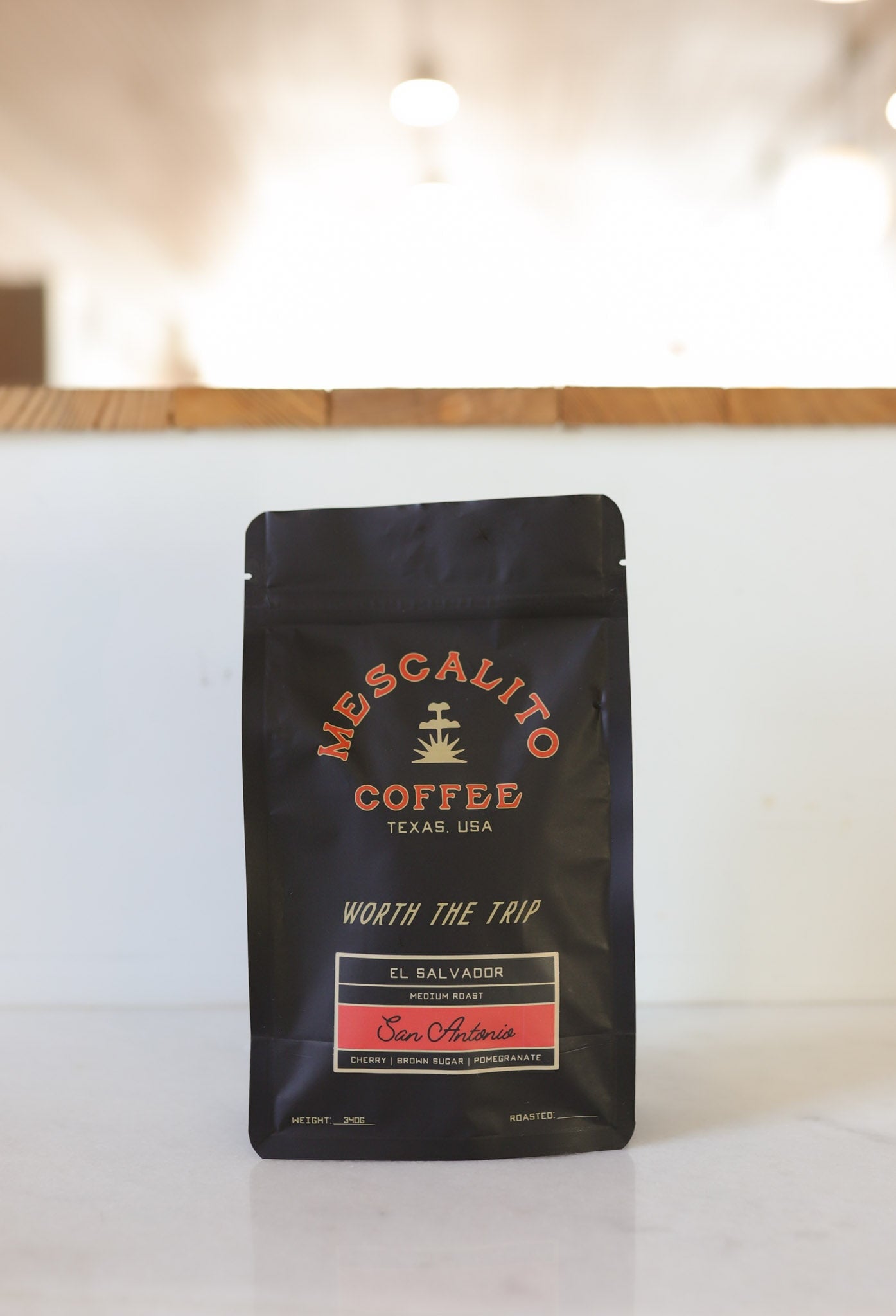 A black bag of Mescalito Coffee’s Blend Whole Coffee Beans from San Antonio rests on a white surface, highlighting rich Pacamara flavors from El Salvador created by anaerobic fermentation. Labeled “Worth The Trip.”.