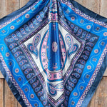 The Rodeo Drive Blue & Purple Paisley Wild Rag is displayed on a wooden surface, showcasing its vibrant paisley pattern.