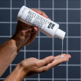 A person pours Blu Atlas Body Wash into their hand from a white bottle against a tiled background.