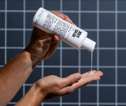 A person pours Blu Atlas Body Wash from a white bottle onto their hand, with a tiled wall in the background.