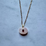 The Boheme Gemstone Pendant Necklace by Jessica Matrasko Jewelry features a gold filled paperclip chain with an oval rose quartz pendant and ruby gemstone—an elegant piece perfect for layering or adding customizable charms.