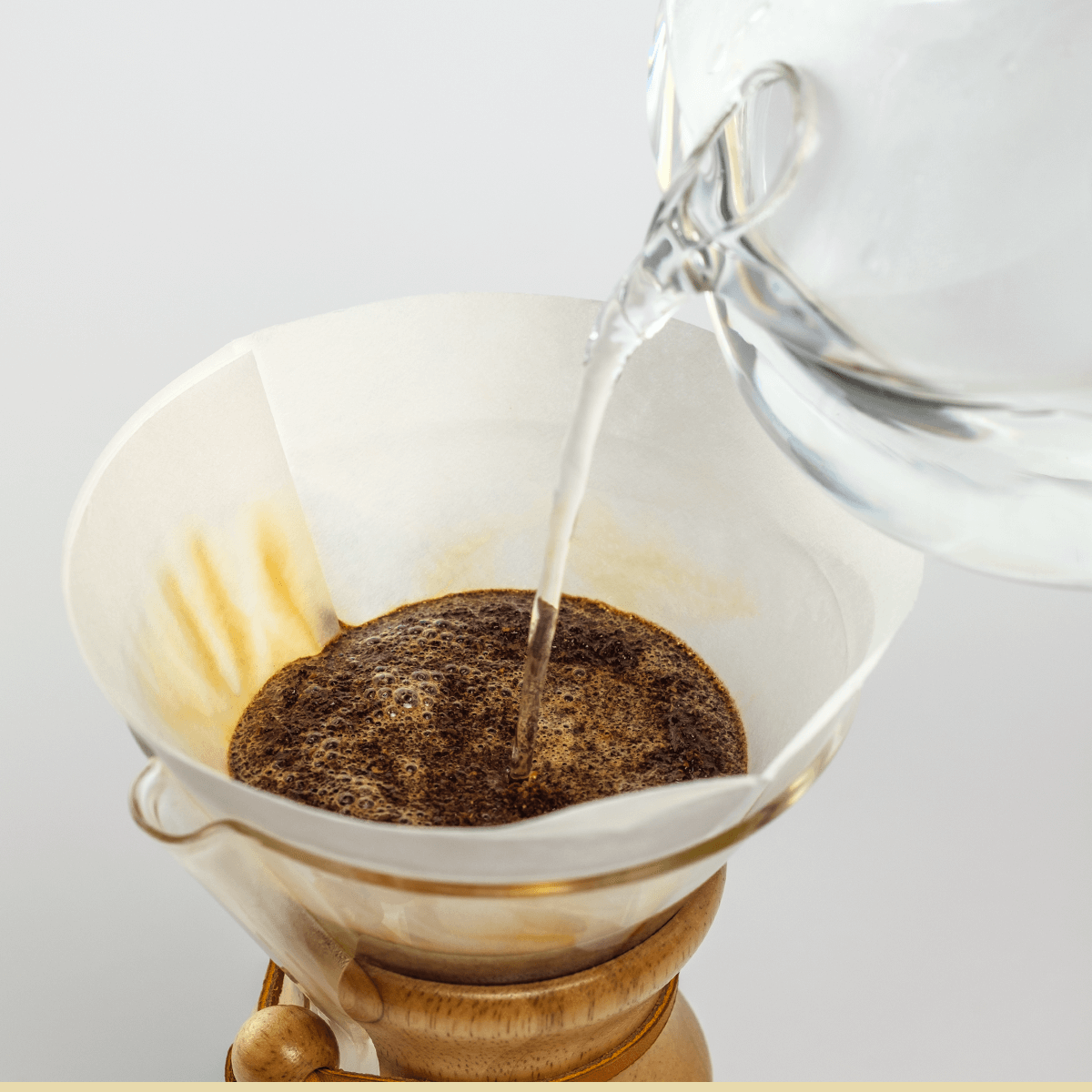 A glass kettle pours hot water over ground coffee in a paper filter inside a Chemex, demonstrating classic pourover brewing with Chemex Bonded Filters | Circle by Chemex.