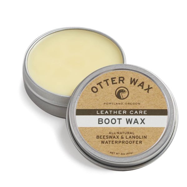 An open tin of Otter Wax Boot Wax displays the label and solid wax inside. The label highlights it as a leather protector made by Otter Wax, featuring beeswax and lanolin for natural waterproofing and leather care.
