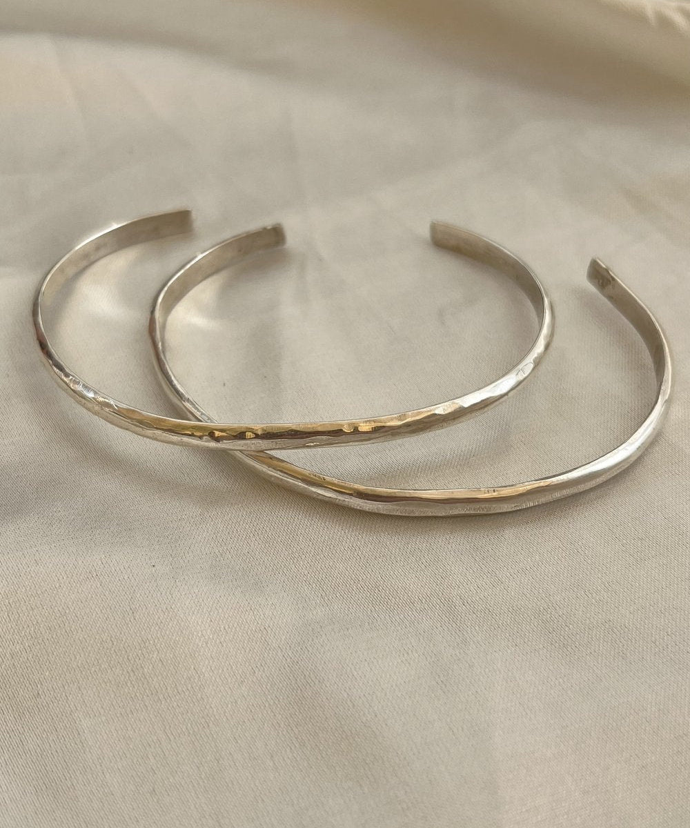 The Simple Silver Hammered Bracelet by Bird of Prey, a small handcrafted piece, is displayed on a light beige fabric surface.