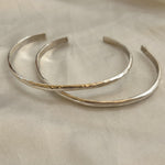 A small, hammered sterling silver bracelet by Bird of Prey is displayed on a light beige fabric background.