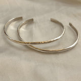 The Simple Silver Hammered Bracelet by Bird of Prey, a small handcrafted piece, is displayed on a light beige fabric surface.