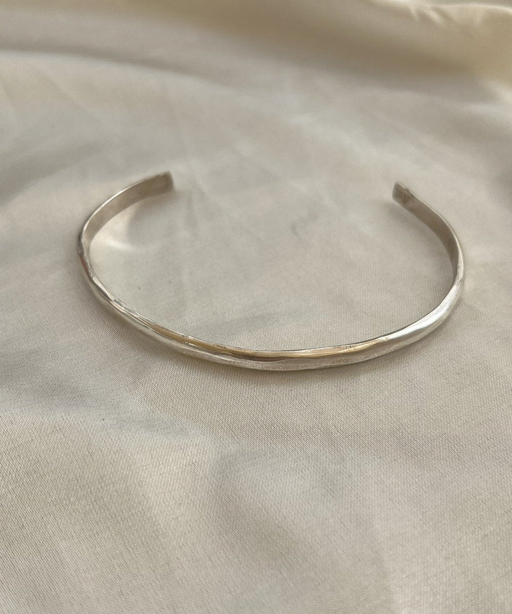 The Bird of Prey Simple Silver Hammered Bracelet, a thin handcrafted sterling silver cuff, is displayed on a light-colored fabric surface.