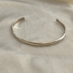 The Bird of Prey Simple Silver Hammered Bracelet (Small) is a thin, handcrafted sterling silver cuff displayed on a light fabric background.