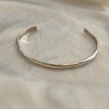 The Bird of Prey Simple Silver Hammered Bracelet, a thin handcrafted sterling silver cuff, is displayed on a light-colored fabric surface.