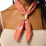 A person styles a pink patterned scarf with the Jenni Earle Brass Bandana Slide over a beige spaghetti strap top, adding a hint of western flair.