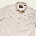 The Broncbuster Snapshirt by Howler Brothers is a beige western shirt with pearl snap buttons and decorative chest stitching, shown laid flat on a light background.