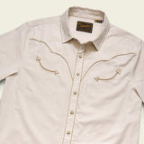 The Broncbuster Snapshirt by Howler Brothers is a beige western shirt with pearl snap buttons and decorative chest stitching, shown laid flat on a light background.