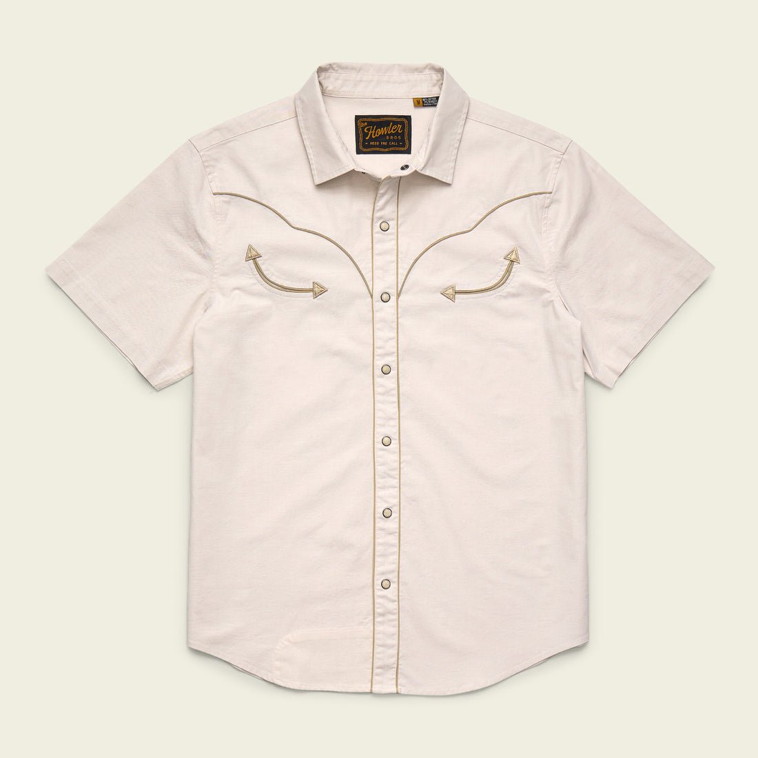 The Howler Brothers Broncbuster Snapshirt is a short-sleeve, light beige western shirt featuring decorative chest stitching, a collar, and classic pearl snap buttons, shown on a plain background.