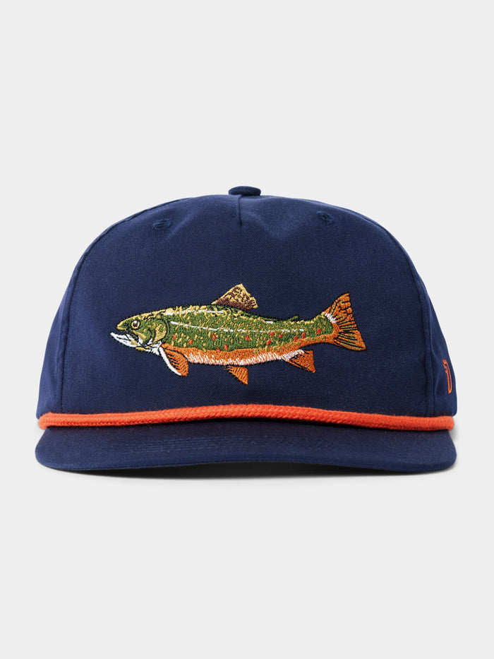 The Brook Trout Hat by Duck Camp features a navy blue snapback design with an embroidered fish on the front, orange trim on the brim, a comfy polyester shell, and an adjustable snapback for the perfect fit.