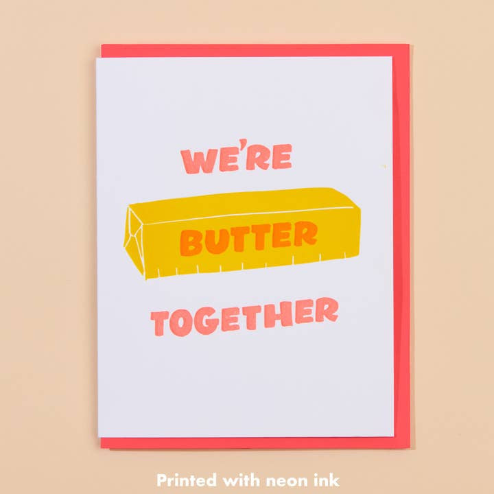 The Butter Together Card by And Here We Are features a stick of butter with "WE'RE BUTTER TOGETHER" in pink and yellow on white—a playful love card for someone special.