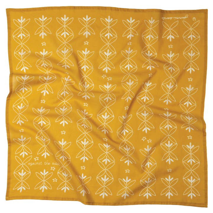 The Jenni Earle Cotton Voile Bandana “Against the Odds” in Saffron is a vintage-inspired square scarf crafted from yellow cotton voile. It features a repeating white floral line pattern, small stars, and cursive text in two corners. Slightly wrinkled for added character, this bandana captures timeless charm in a classic style.