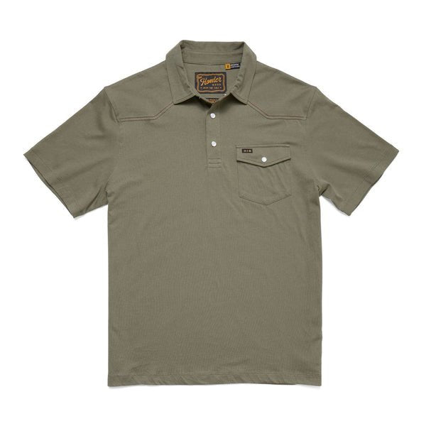 The Ranchero Polo by Howler Brothers is an olive green short-sleeve shirt featuring a chest pocket, three-button placket, Western yokes, and a branded label at the collar.