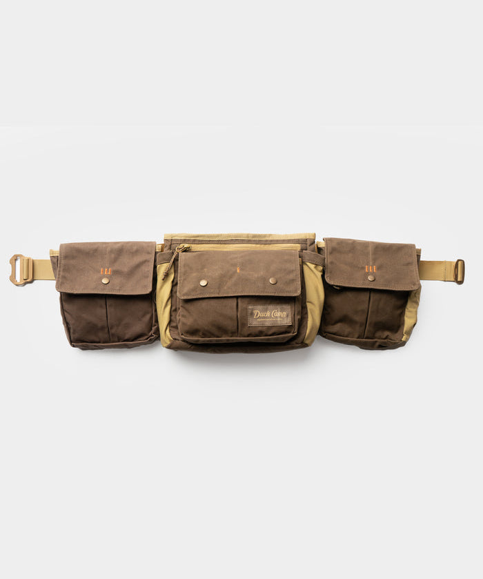 The Duck Camp Canvas Shell & Game Bag is a brown waxed canvas waist bag with buckle closure, two side pouches, and a central zippered pocket—perfect for the range or hunting—shown on a white background.