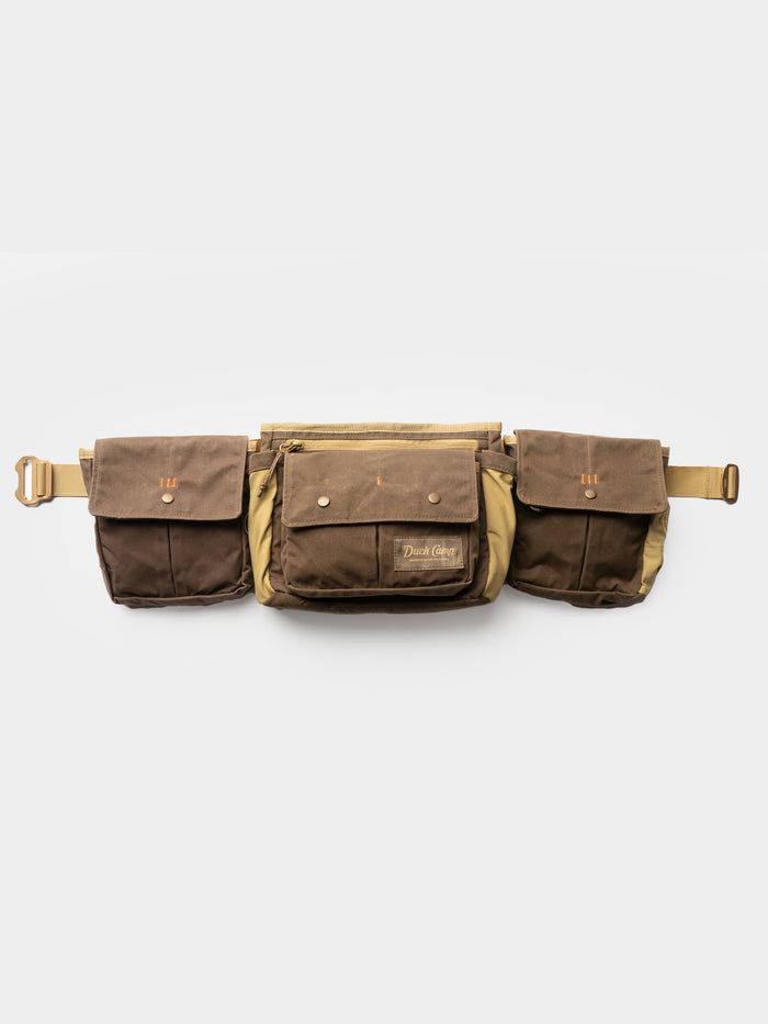 The Duck Camp Canvas Shell & Game Bag is a brown waxed canvas waist bag with buckle closure, two side pouches, and a central zippered pocket—perfect for the range or hunting—shown on a white background.