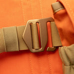 Close-up of a brown plastic buckle fastened on a tan strap against orange fabric, featured on the Duck Camp Canvas Upland Strap Vest.